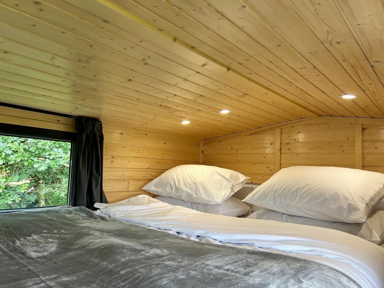 Een houten kamer met twee bedden, een groot raam en uitzicht op groen.