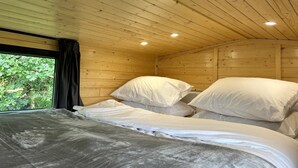Ein Zimmer in einer Holzhütte mit zwei Betten, einem großen Fenster und Blick ins Grüne.