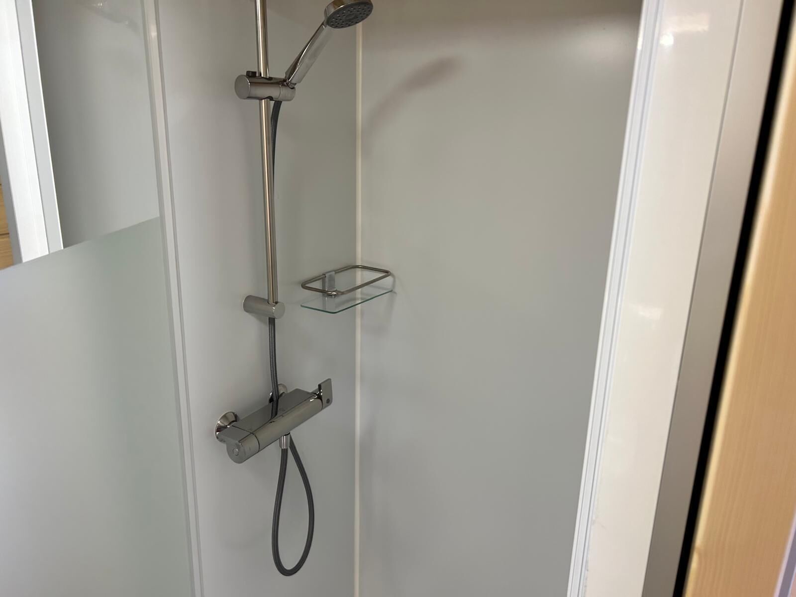 Una ducha moderna con un cabezal de ducha manual, un accesorio de ducha manual y un estante de vidrio.