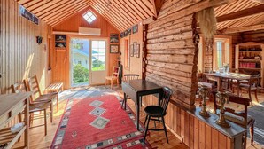 Interior de una cabaña de troncos con comedor, un ventanal y vistas al exterior.