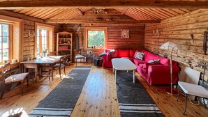Interior acogedor de una cabaña con techo de madera, un sofá rojo, una mesa de comedor y una estantería.
