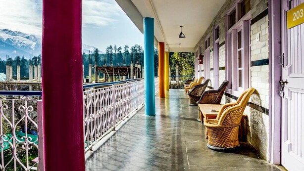 A covered outdoor area with wicker furniture, a view of mountains, and a building with a number sign. - Oak Land House (Manali)