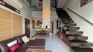 A modern living room with a sofa, a coffee table with a decorative bowl, a staircase, and a kitchen area in the background. - 3bedroom Penthouse at Asiana Villas  (Boracay Island)