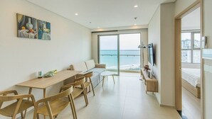 A modern living room with a wooden dining table, a sofa, and a large window overlooking the sea.