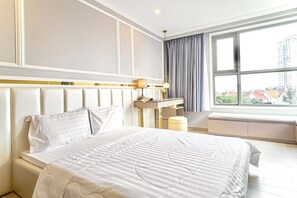 A hotel room with a large bed, a desk, and a window with a view of buildings. - SeaStay Condotel The Song Vung Tau (Ho Chi Minh City)