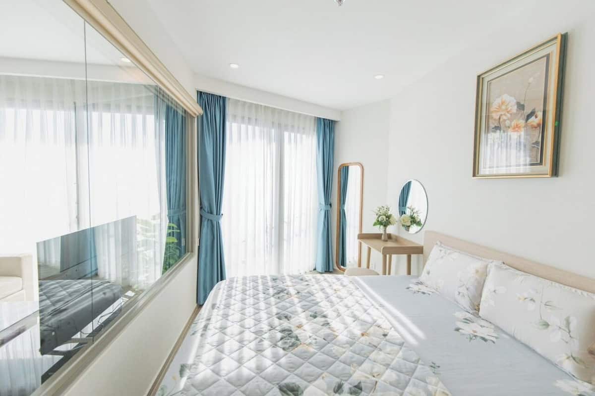 Quarto de hotel com uma cama grande, mesa de cabeceira com espelho e janela com cortinas.
