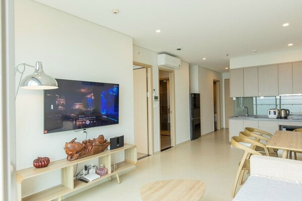 A modern living room with a flat-screen TV, wooden entertainment unit, and a dining area with a wooden table and chairs. - SeaStay Condotel The Song Vung Tau (Ho Chi Minh City)