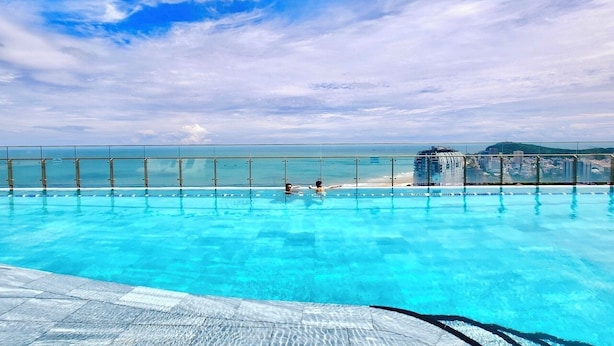 A swimming pool with clear blue water, a glass barrier, and a view of the beach and city skyline.