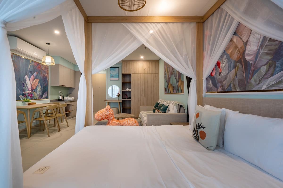 Quarto com cama de dossel, escrivaninha com cadeiras, sofá e área de jantar.