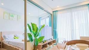 A modern hotel room with a bed, a dining table with cutlery, a potted plant, and a large window with curtains.