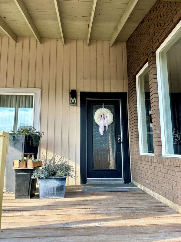 A wooden porch with a black door, potted plants, and a brick wall.