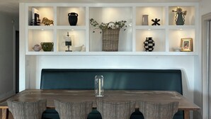A dining area with a wooden table and grey upholstered chairs, a dark green bench, and a wall-mounted shelf with various decorative items. - The Treehouse: Spacious Retreat with Theater Room, Fire Pit & Mountain Views (Orem)