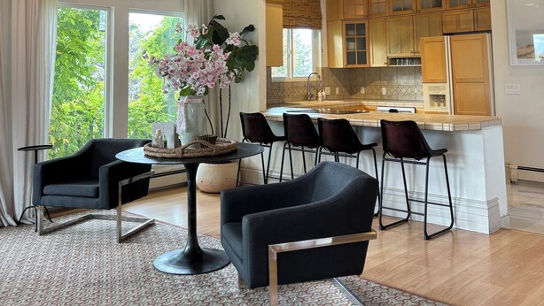 A modern kitchen with wooden cabinets, a central island with bar stools, and a dining area with a round table and chairs. - The Treehouse: Spacious Retreat with Theater Room, Fire Pit & Mountain Views (Orem)