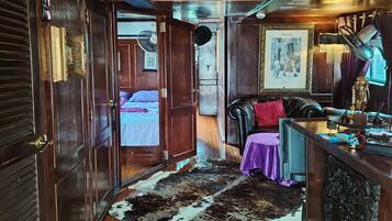 A narrow hallway with wooden doors, a cowhide rug, a patterned rug, a bed with a purple bedspread, a leather sofa, and a bar area with a fan and decorative items.