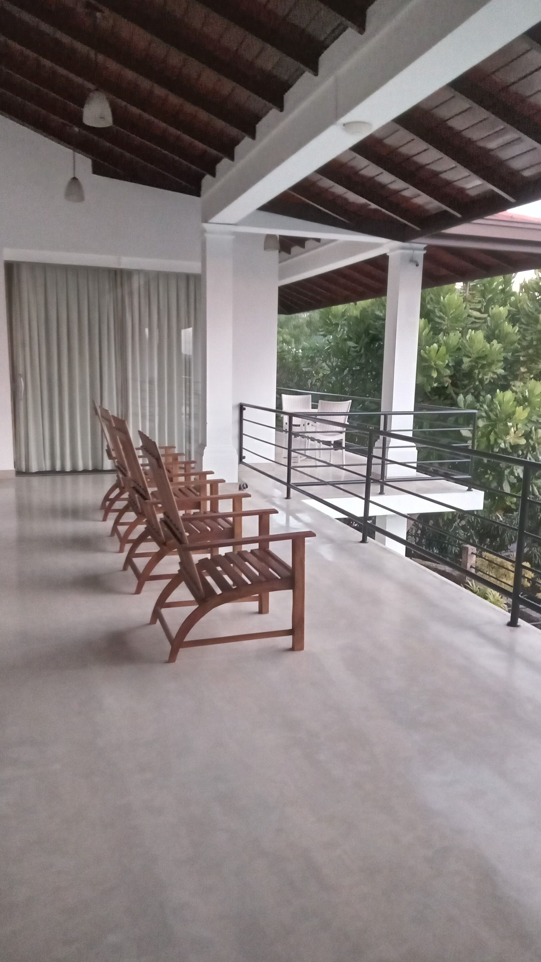 Un espace extérieur aménagé avec des meubles de jardin en bois, comprenant des chaises et des tables, un balcon doté d’une balustrade et offrant une vue sur la verdure.