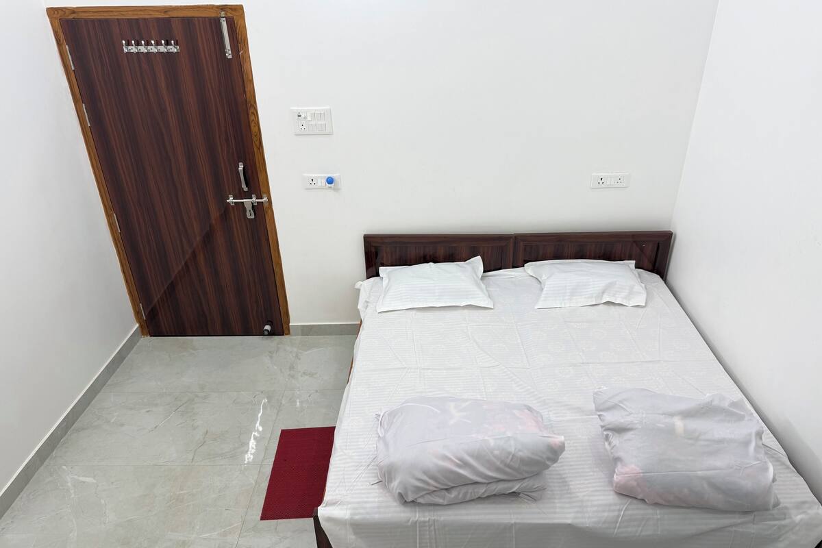 A bedroom with a wooden door, a bed with white bedding, and a red rug on the floor.