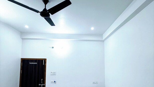 A bedroom with a bed, a ceiling fan, and a door. - Rameshwaram Stay (Faizabad)