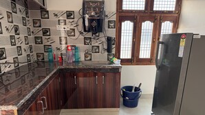A kitchen with dark wooden cabinets, a marble countertop, a stainless steel refrigerator, and a window with wooden frames. - Rameshwaram Stay (Faizabad)