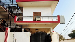 A two-story building with a red and white facade, a gated entrance, and a staircase leading to the upper floor. - Rameshwaram Stay (Faizabad)