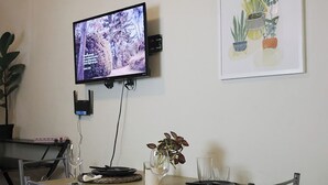 A dining area with a TV mounted on the wall, a table set with plates, a vase with flowers, and a framed plant illustration on the wall.