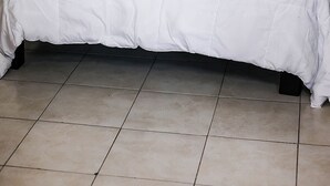 A neatly made bed with a white duvet and grey patterned pillows, a bedside lamp, and a dark headboard.