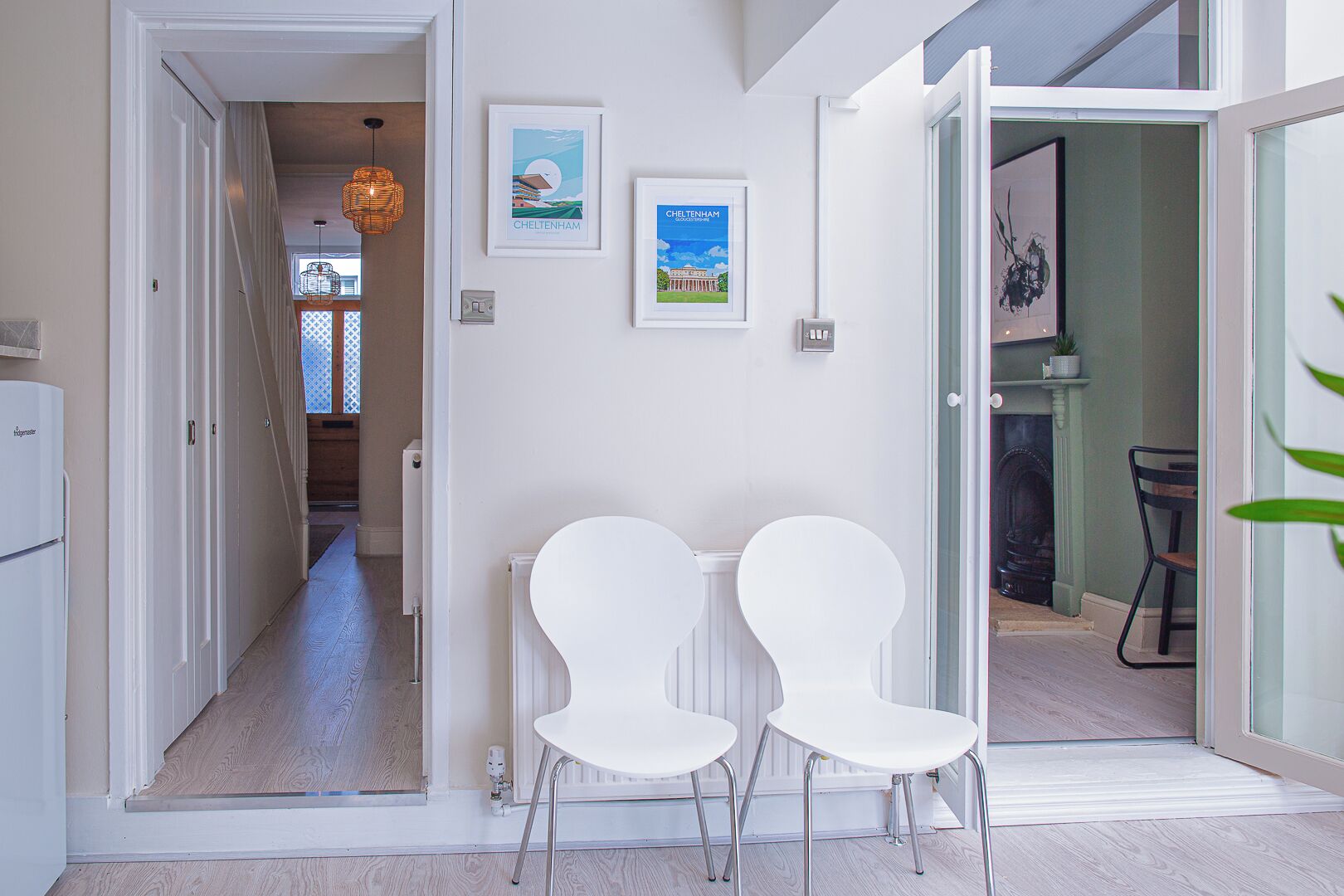 A hallway with a white radiator, two white chairs, and framed pictures on the wall.