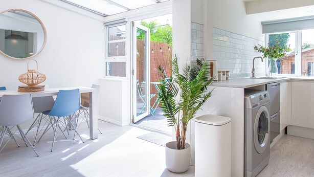 Una cucina moderna con lavatrice integrata, zona pranzo con tavolo e sedie, e un'ampia finestra che garantisce luce naturale.