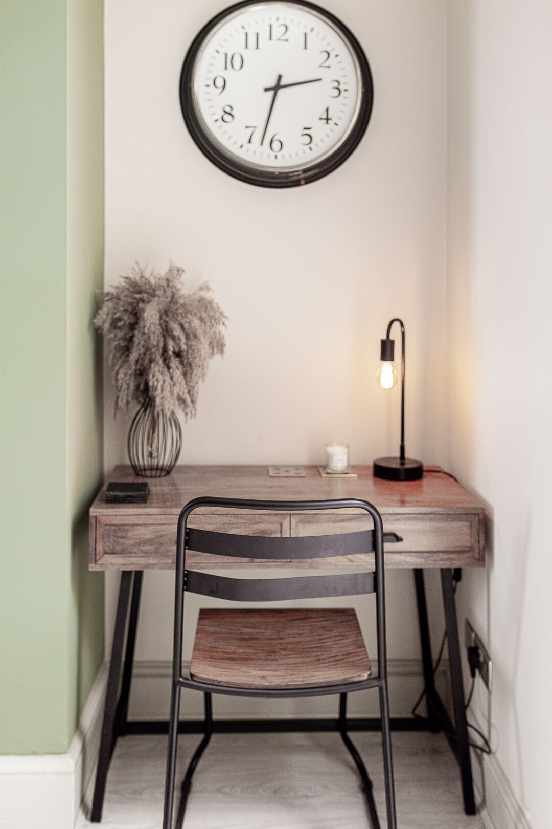 Un bureau avec une horloge, une chaise, une lampe et un vase contenant des plantes séchées.