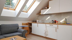 A compact kitchen with a skylight, a dining area with a table and chair, and a gray sofa. - Cozy apartment in Dziwnów with WiFi (Dziwnów)