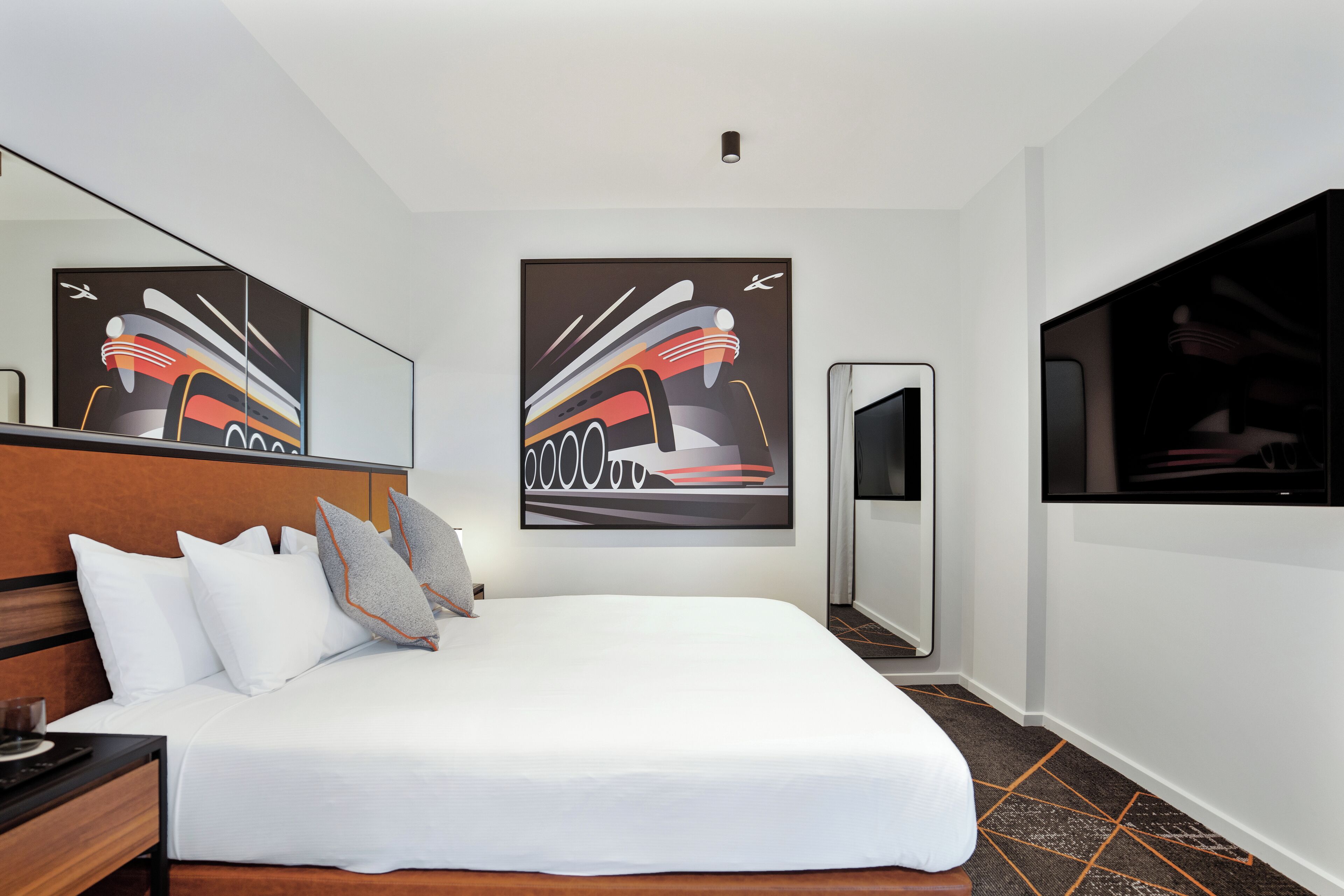 Ein Hotelzimmer mit einem großen Bett, einem Holzkopfteil, einem Flachbildfernseher und zwei abstrakten Bildern an der Wand.