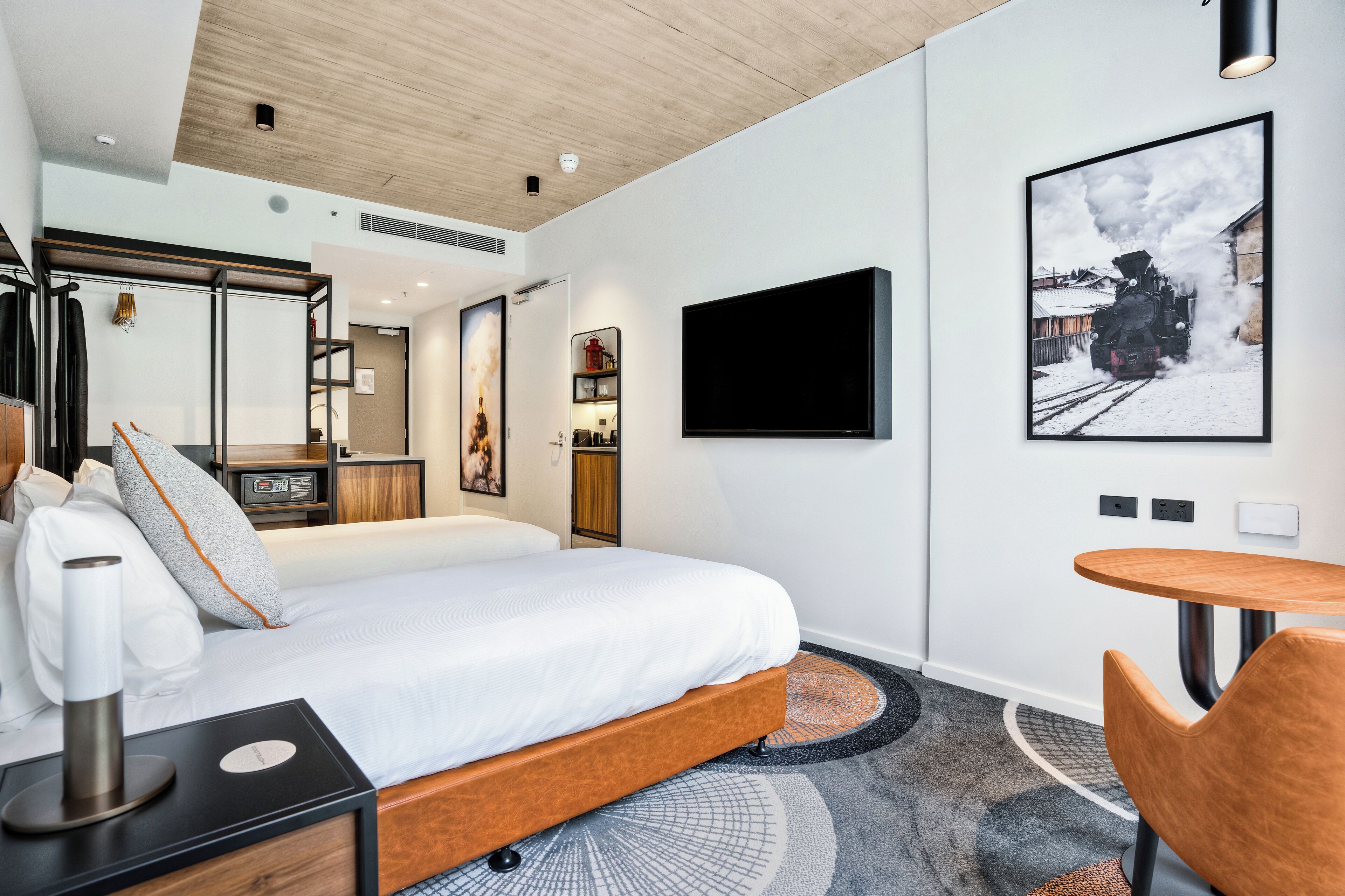 Une chambre d’hôtel moderne équipée d’un lit, d’une table de chevet, d’une chaise, d’un téléviseur et d’un tableau encadré au mur.
