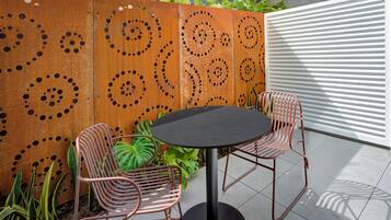 A patio area with a round table and two chairs, a decorative metal wall with circular patterns, and a white slatted wall.