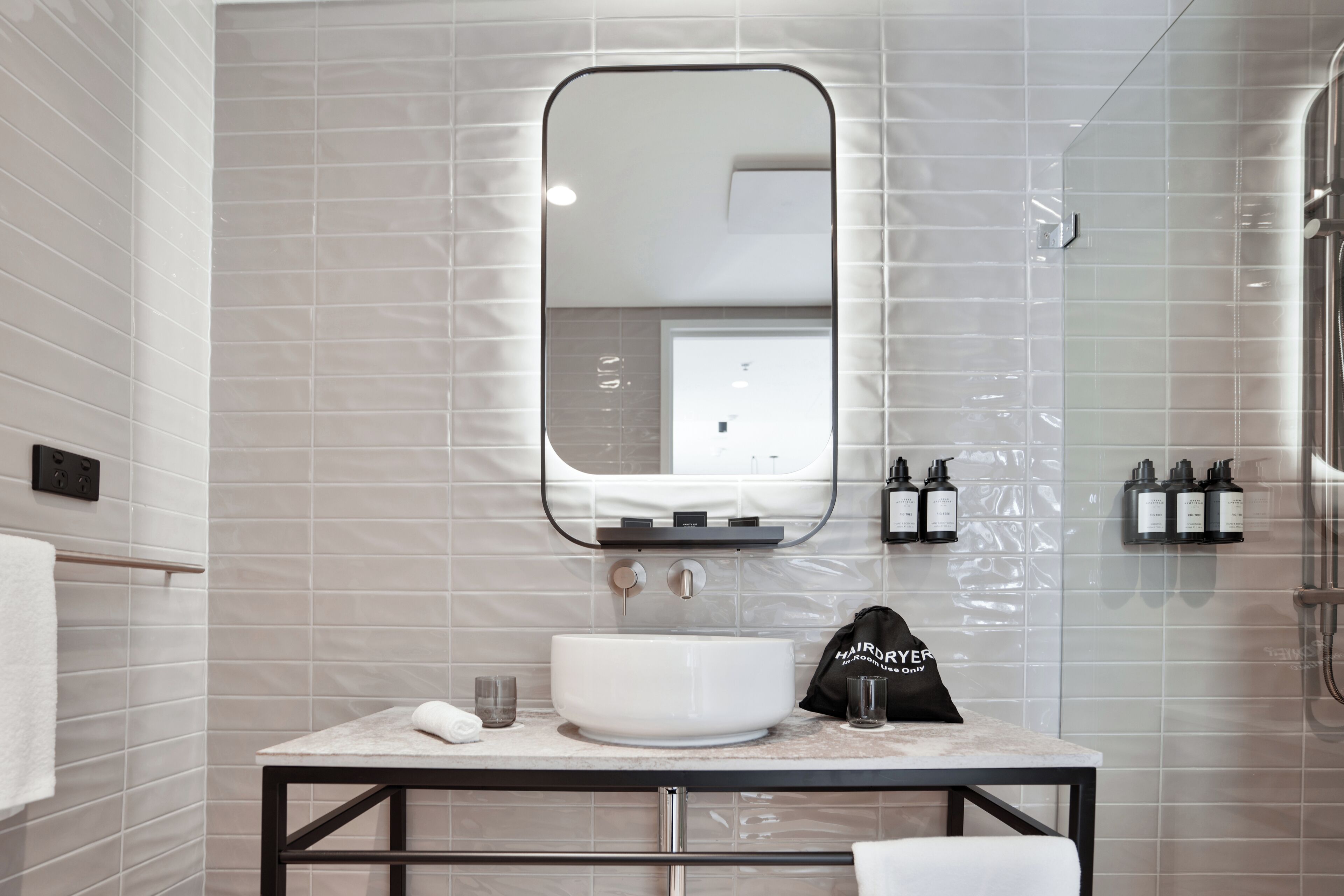 A modern bathroom with a white sink, a large mirror, and a towel rack.