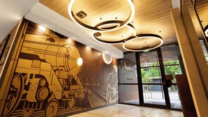 A hotel lobby with a large mural of a train and tracks, modern circular ceiling lights, and a glass door entrance. - Hoteloco (Alexandria)