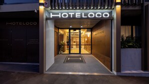 The entrance to a hotel named HOTELLOCO with a modern design, featuring a glass door and illuminated signage. - Hoteloco (Alexandria)