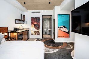 A modern hotel room with a bed, a desk, a kitchenette, and a bathroom. There are posters on the walls and a TV mounted on the wall. - Hoteloco (Alexandria)