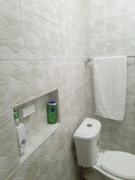 Un baño con un inodoro, una toalla colgada en un perchero y un estante con artículos de aseo.