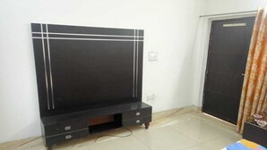 A room with a black entertainment unit, a tiled floor, and a colorful bedspread. - G G Multi Complex (Sardhana)