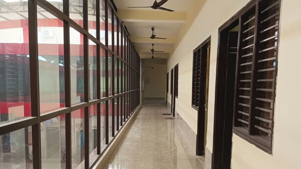 A corridor with large windows, ceiling fans, and a tiled floor. - G G Multi Complex (Sardhana)