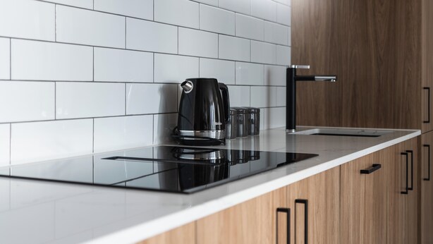 A modern kitchen with a black coffee maker, a glass, and a kettle on a sleek countertop. - Luxury Apartment on Stuart Street (Dunedin)