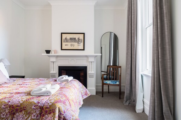 A hotel room with a bed, a fireplace, a chair, and a large mirror. - Luxury Apartment on Stuart Street (Dunedin)