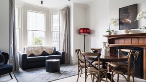 A living room with a sofa, a coffee table, a dining table with chairs, a fireplace, and a lamp. - Luxury Apartment on Stuart Street (Dunedin)