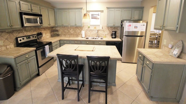 A kitchen with a central island, two chairs, a microwave, stove, sink, and a refrigerator. - Cozy Cove Grand Lake Home - Near cove with ramp (Vinita)