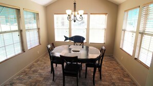 A dining area with a round table, four chairs, a chandelier, and large windows with blinds. - Cozy Cove Grand Lake Home - Near cove with ramp (Vinita)