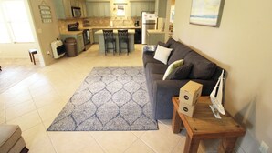 A spacious living area with a grey sofa, a patterned rug, and a wooden coffee table. There is a kitchen in the background with green cabinets and a large island. - Cozy Cove Grand Lake Home - Near cove with ramp (Vinita)