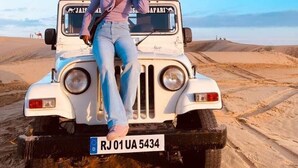 A person posing on a white safari vehicle with a license plate RJ01 UA 5434 in a desert setting. - Robin Desert Safari Camp  (Jaisalmer)