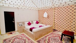 A bedroom with a bed, a small table, a window, and patterned walls. - Robin Desert Safari Camp  (Jaisalmer)
