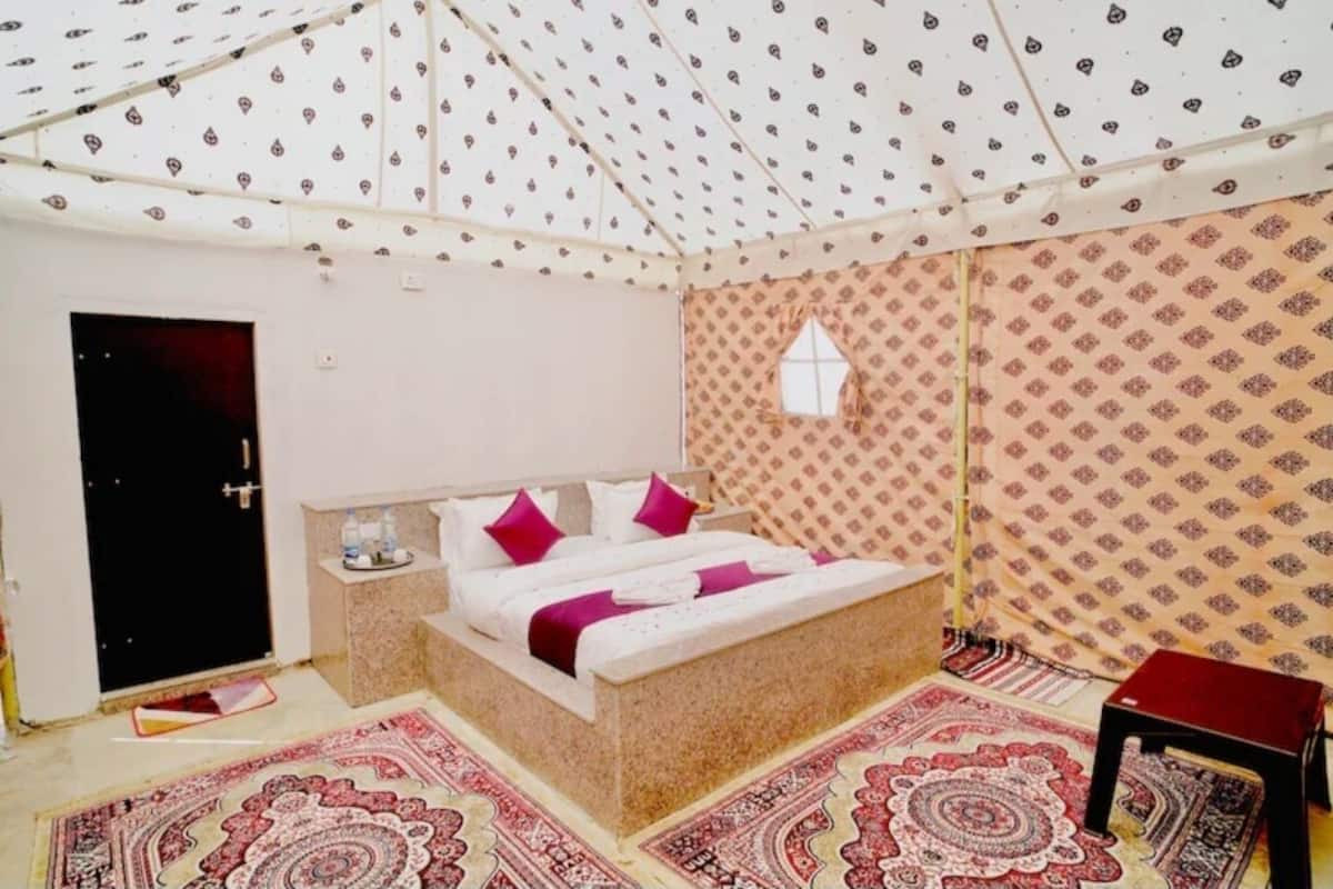 A bedroom with a bed, a small table, a window, and patterned walls.