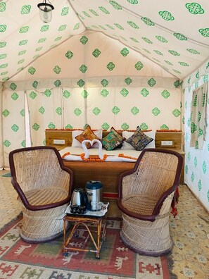 Ein Zeltraum mit einem Bett, zwei Korbstühlen, einem kleinen Tisch mit Wasserkocher und Tassen sowie gemusterten Vorhängen.