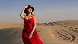 A person in a red dress standing in a desert with sand dunes in the background. - Robin Desert Safari Camp  (Jaisalmer)
